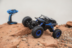 An RC off-road rock crawler car on terracotta-toned rocky terrain with a soft charcoal shadow, against a blurred bright white